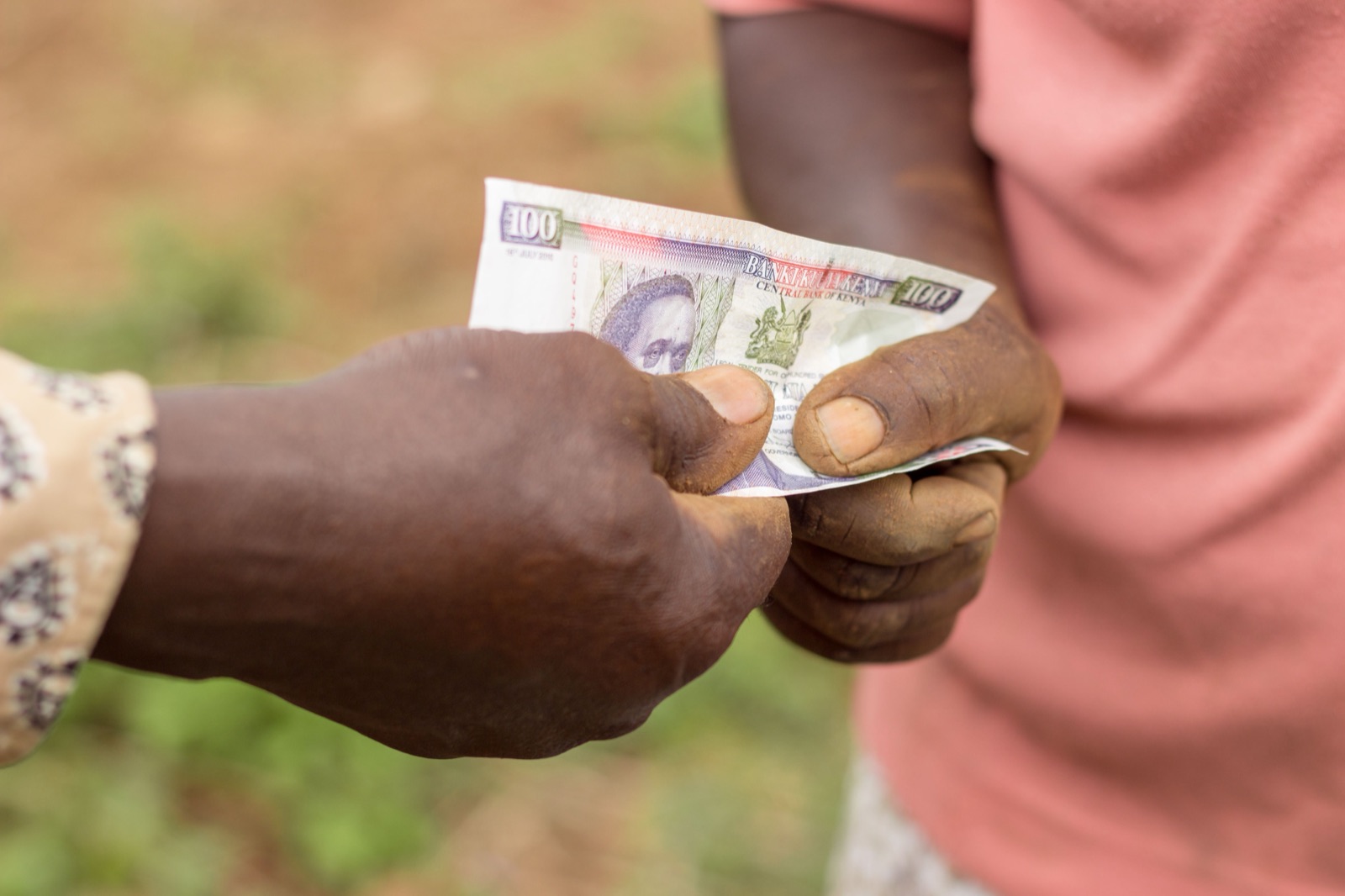 Two hands passing a one hundred shilling note.